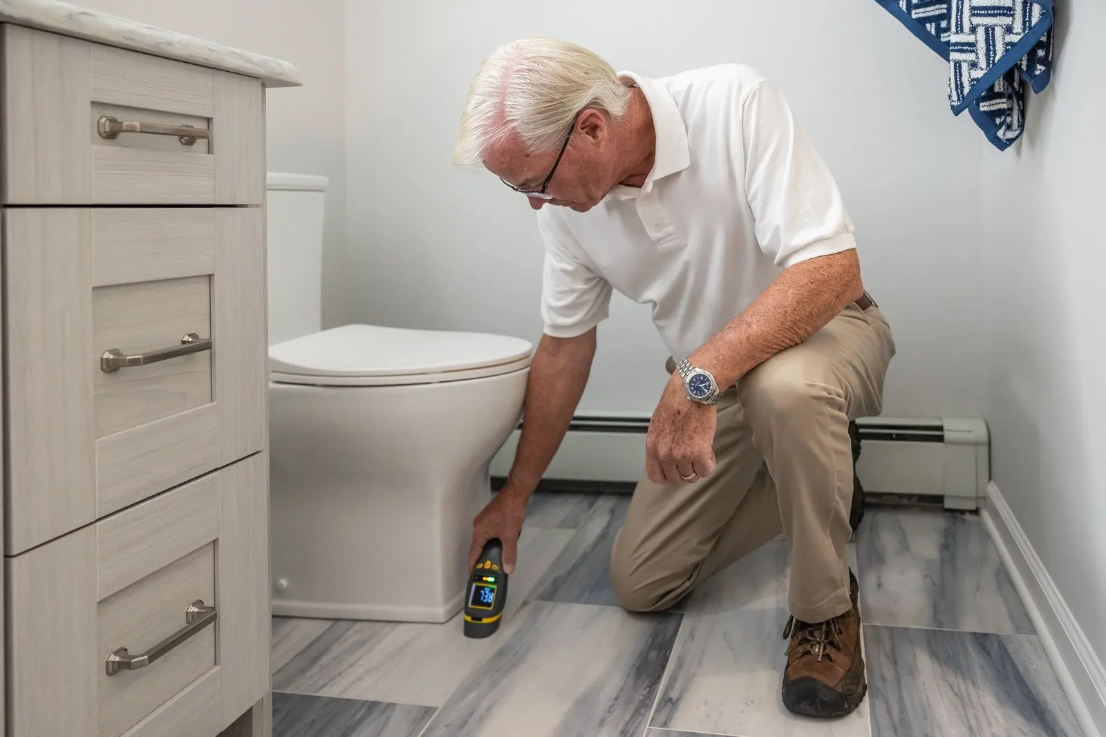 Inspector kneeling in a bathroom using a handheld device to check for moisture