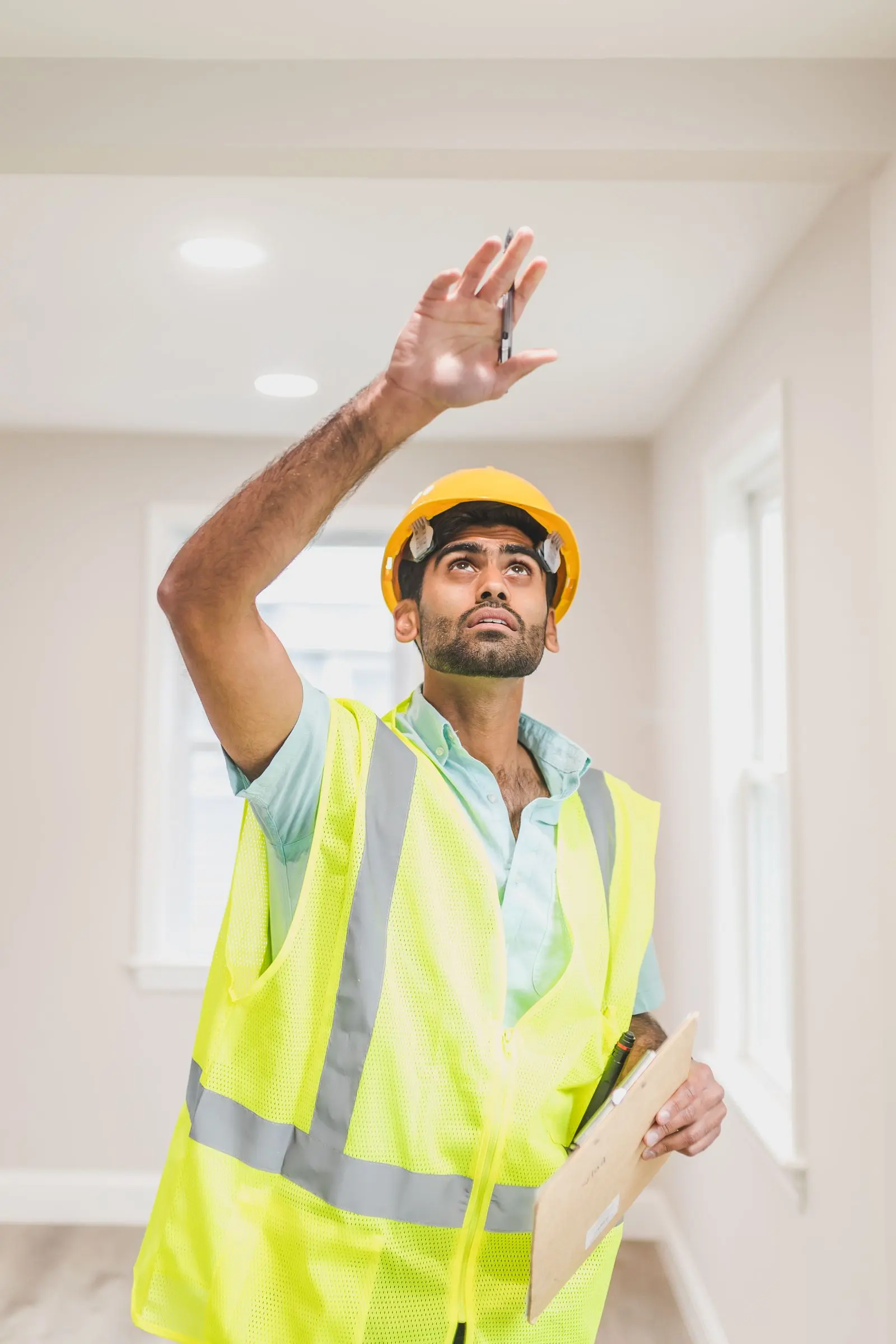 Home inspector in a hard hat and safety vest looking up to inspect a ceiling
