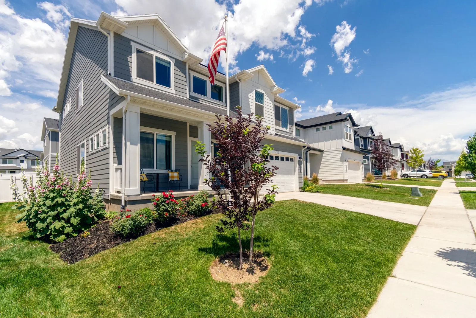 Two-story gray suburban home with an American flag and a landscaped lawn