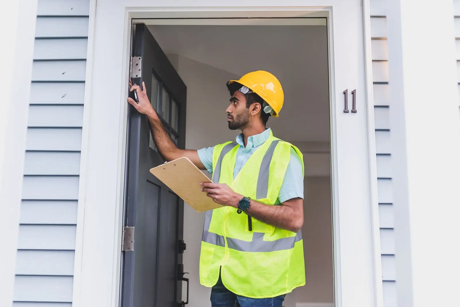 Home inspector in a hard hat checking a front door and frame