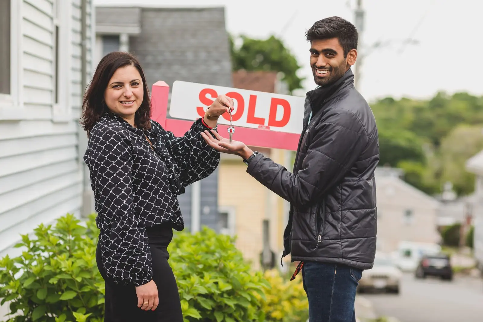 Realtor and a new owner holding a Sold sign in front of a house